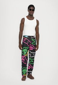 Black denim pants featuring colorful cartoon patterns in pink, green, blue, and yellow, paired with a white tank top and sunglasses.