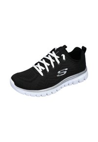 Zapatilla deportiva ligera negra con cordones blancos y suela blanca gruesa, que presenta un logo plateado en el costado y una parte superior de malla transpirable.