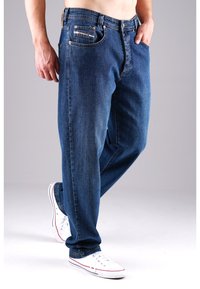 Blaue Jeans im Straight-Leg-Design mit Knopfverschluss, fünf Taschen und kontrastfarbenen Nähten, getragen mit weißen Turnschuhen.