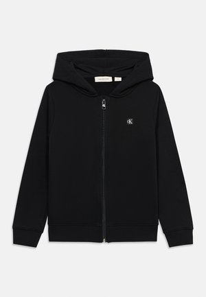 Sweat à capuche zippé noir avec manches longues, poignets côtelés, capuche et petit logo blanc "cK" sur le côté gauche de la poitrine.
