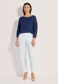 Marineblauwe gebreide trui met een brede halslijn, gecombineerd met lichtblauwe op maat gemaakte broeken en beigekleurige hoge hakken, voorzien van opgerolde manchetten.