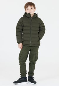 Grön puffjacka med huva, dragkedjestängning och ribbade ärmslut. Matchat med gröna cargobyxor med sidofickor. Svarta sneakers.