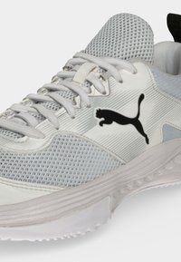 Λευκό και γκρι αθλητικό παπούτσι Puma με διχτυωτό ύφασμα, κορδόνια και μαύρο λογότυπο Puma στο πλάι, εμφανίζεται από γωνιακή κοντινή λήψη.