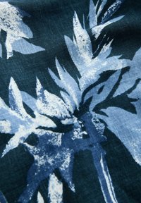 Floral-patterned fabric in deep blue and light blue tones. Features abstract leaf shapes with a textured appearance on a dark background.