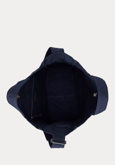 Τσάντα ώμου από σκουρό μπλε ύφασμα με φαρδιά θήκη, ρυθμιζόμενο λουρί, εσωτερική τσέπη με φερμουάρ και κλείσιμο με κουμπί πάτημας.