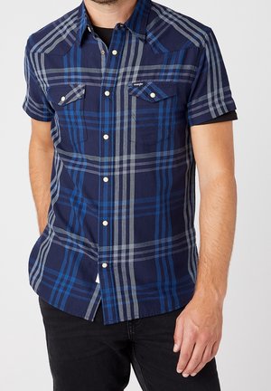 Camisa de cuadros de manga corta en tonos azul marino y azul, con cierre de botones, dos bolsillos en el pecho y un tejido ligero con una textura suave.