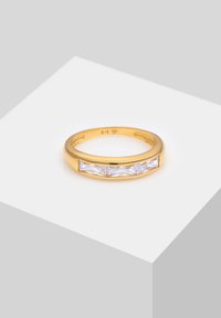 Anillo de oro con una banda lisa y tres piedras rectangulares transparentes dispuestas en fila, mostrando un diseño elegante y pulido.