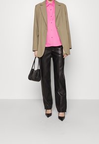 Blazer oversize beige, camicia button-up fucsia brillante, pantaloni in pelle nera a gamba dritta e una piccola borsa nera. Tacchi a punta neri completano il look.