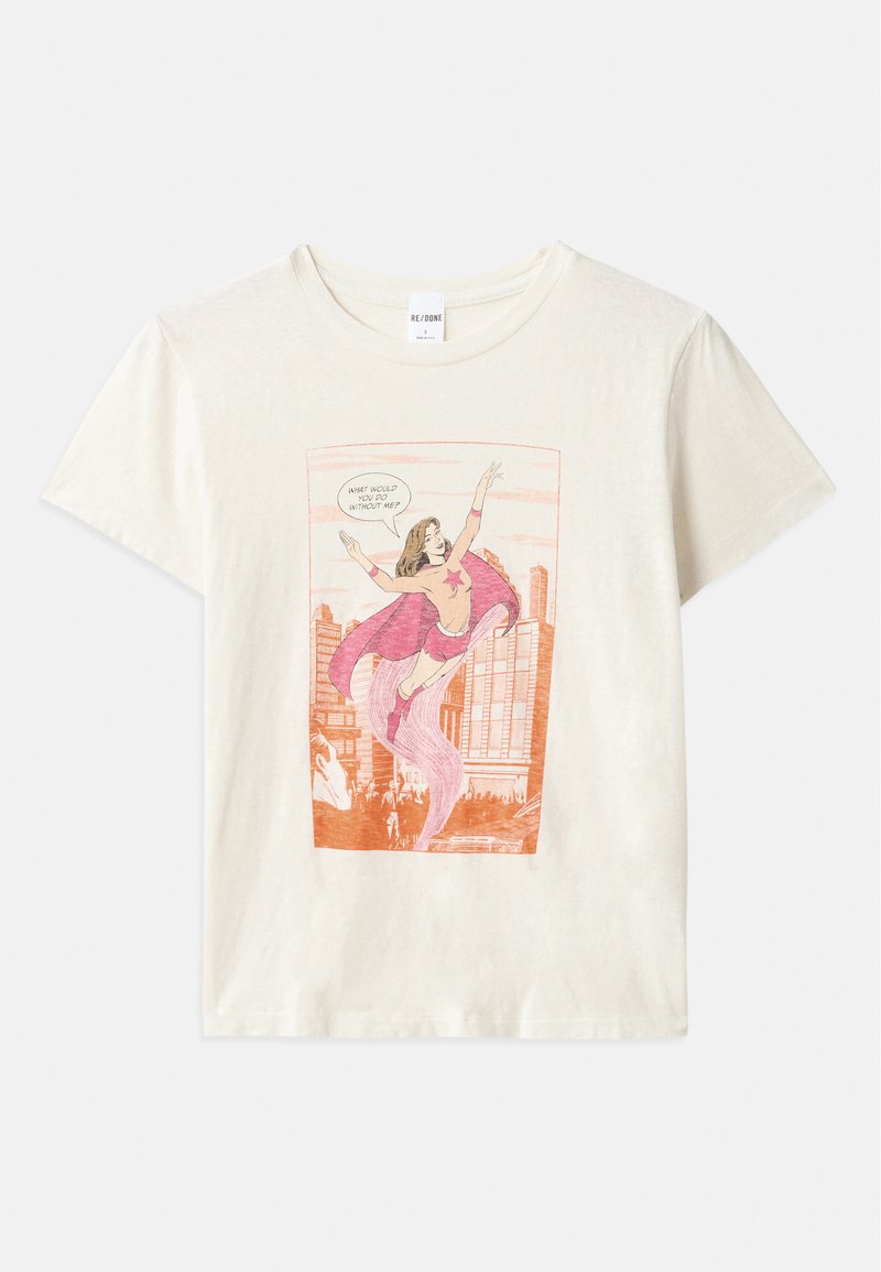 T-shirt in cotone color crema con una grafica in stile fumetto di una donna in un costume rosa con un mantello, circondata da uno sfondo di skyline cittadino.
