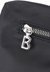 Schwarze Textiltasche mit einem silbernen Reißverschlussgriff, auf dem der Buchstabe "B" eingraviert ist, sowie einer strukturierten Oberfläche. Die Nahaufnahme hebt das Reißverschlussdetail hervor.
