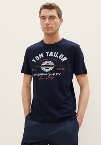Navy blue cotton t-shirt featuring a round neck, short sleeves, and a front print with the text "Tom Tailor" and decorative elements.