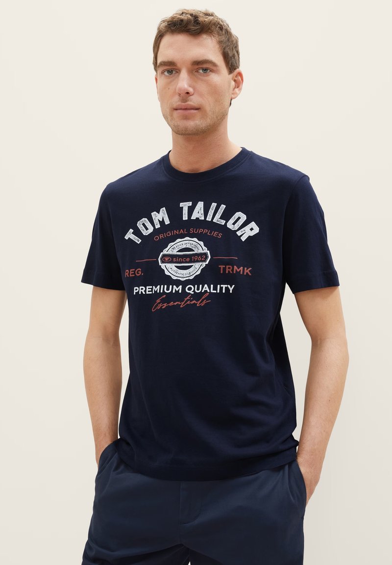 Navy blue cotton t-shirt featuring a round neck, short sleeves, and a front print with the text "Tom Tailor" and decorative elements.