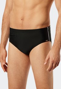 Schwarze Schwimmbriefer mit glatter Textur, ausgestattet mit einer seitlichen Reißverschlusstasche, kontrastierenden Paspeln an den Seiten und einem niedrigen Bund.