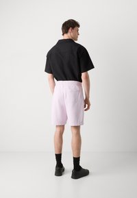 Kortærmet sort struktureret skjorte med krave, parret med lys rosa shorts med elastisk talje og sorte sko med sokker.