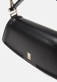 Borsa a mano in pelle nera con una forma strutturata, caratterizzata da un accento in metallo dorato e una tracolla removibile per una maggiore versatilità nel trasporto.
