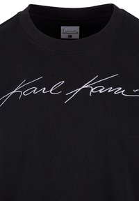 Sweatshirt noir à col rond avec une broderie en écriture cursive blanche "Karl" sur le devant. Le tissu semble doux et lisse.