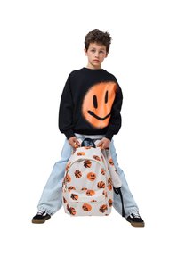Čierna mikina so vzorom oranžového smajlíka, svetlomodré džíny a biely ruksak s oranžovým smajlíkom a vzorom basketbalových loptičiek. Čierne tenisky.