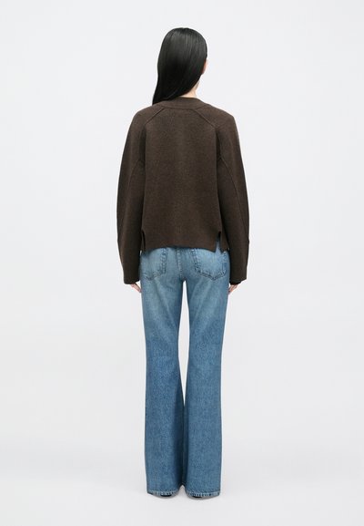 Pruun heegeldatud kampsun, millel on lõdvestunud lõige ja külgmised lõhikud. Kandke seda helesiniste laiade teksapükstega, mis näitavad klassikalist teksariide tekstuuri.