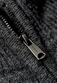 Primo piano di un tessuto a maglia nero con una zip inclinata e un tirante testurizzato, che evidenzia una consistenza morbida e pelosa e cuciture dettagliate.