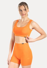 Fel oranje sportbeha en shorts met hoge taille van rekbaar materiaal, voorzien van een gladde textuur en logo-accenten.