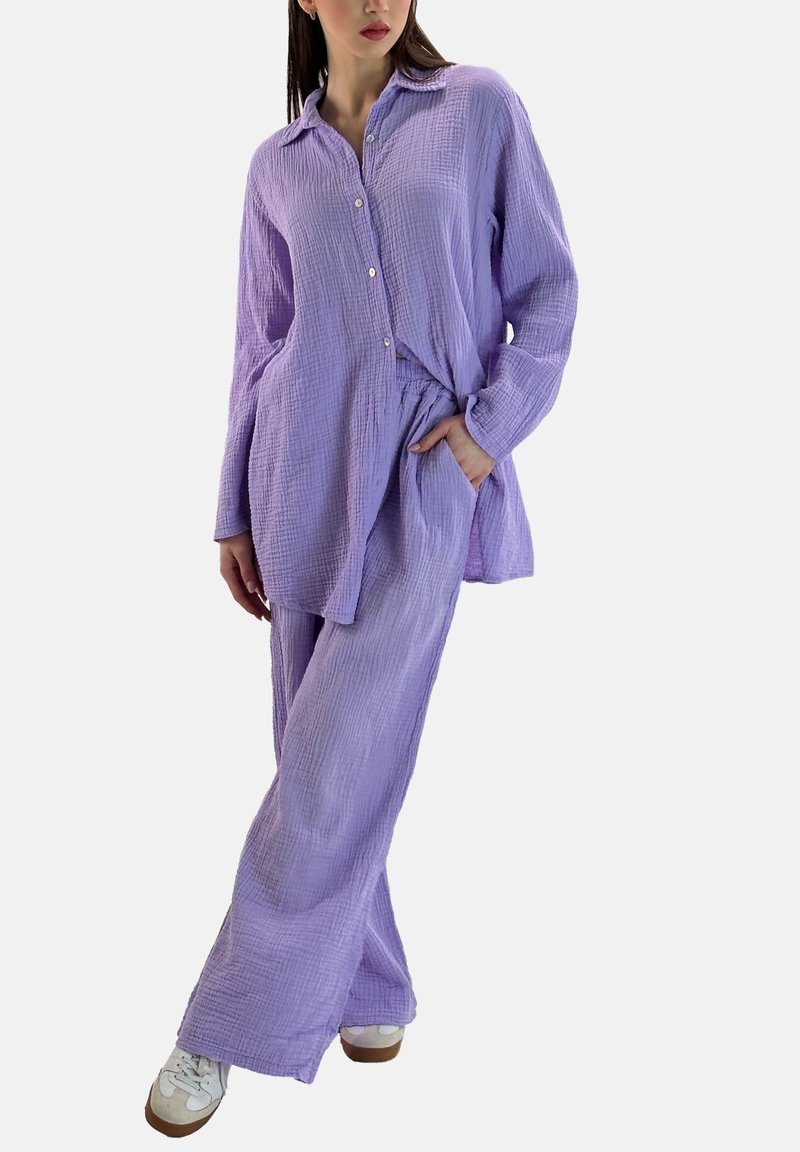 Conjunto coordinado que incluye una camisa de botones de lavanda ligera y texturizada, junto con pantalones anchos a juego, complementados con zapatillas blancas.
