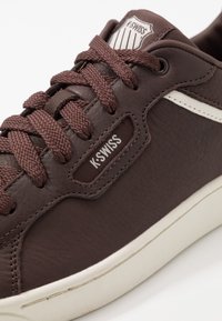 Baskets en cuir marron avec finition texturée, lacets marron tissés et accents blancs. Présente le logo K-Swiss près du haut.