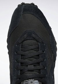 Chaussure de sport noire avec textures en mesh et suède, lacets croisés et semelle en caoutchouc visible en haut.
