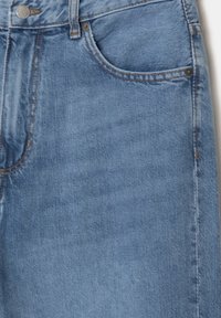 Jean en denim bleu clair avec un design classique à cinq poches, une texture délavée et des coutures contrastées sur les coutures. Fermeture par bouton en métal visible.
