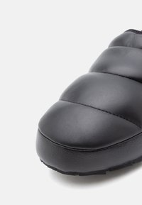 Fekete bőr slip-on cipő, steppelt dizájnnal, kerek orral, texturált felülettel és alacsony profilú gumitalppal.