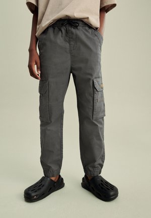 Grijze cargobroek met een elastische tailleband, zijzakken en opgefranste enkels, gecombineerd met zwarte geperforeerde instappers.