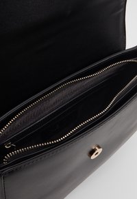 Borsa a tracolla nera in pelle con chiusura a zip, tasche interne e texture liscia. Presenta dettagli in metallo dorato e un design minimalista.