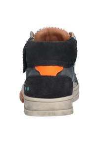 Zwarte suède sneakers met een bruine binnenkant, oranje accenten op de hiel en een rubberen zool. Voorzien van een klittenbandsluiting. Textuurdetail aan de achterkant.