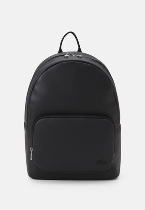 Schwarzer Leder-Rucksack mit einer vorderen Reißverschlusstasche, einem oberen Griff und silbernen Reißverschlusszügen vor schlichtem weißem Hintergrund.