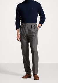 Laivastonsininen pooloneule yhdistettynä vaaleanharmaisiin laskostettuihin housuihin. Asun täydentävät ruskeat nahkakengät, jotka korostavat räätälöityä istuvuutta.