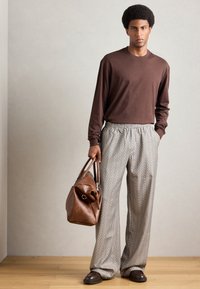 Chemise brune à manches longues, pantalon clair à motifs et sac en cuir marron. Le modèle porte des chaussures foncées ; conception à panneau plat, coupe décontractée.