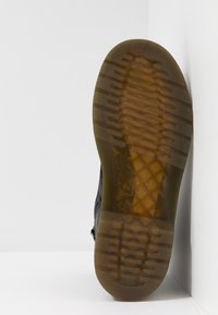 Semelle de chaussure noire avec une surface en caoutchouc texturé, présentant un motif en nid d'abeille et des rainures horizontales pour une meilleure adhérence. Les bords sont légèrement arrondis.