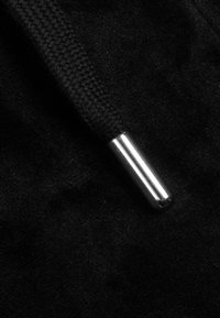 Detailní záběr černé splétané tkaničky s lesklým stříbrným kovovým zakončením na černém látkovém pozadí.