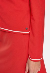 Red sweater with a smooth texture, featuring white accent stripes on the cuffs and a small logo detail on the side.