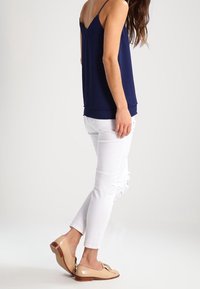 Haut sans manches bleu marine avec un col en V et une coupe décontractée, associé à un jean skinny blanc déchiré et des ballerines beige avec un détail nœud.