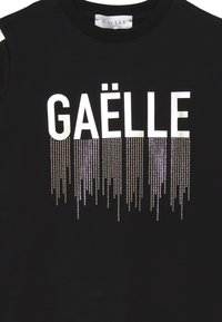 Felpa nera con la parola "GAËLLE" in grassetto lettere bianche, impreziosita da una gradazione di perline metalliche che creano un effetto goccia.