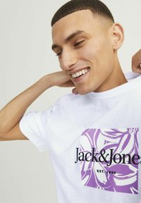 Hvid kortærmet t-shirt med et lilla blomstermotivet og teksten "Jack & Jones" samt "EST. 1990", lavet af bomuldsmateriale og i afslappet pasform.