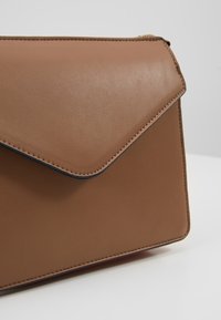 Borsa a busta in pelle marrone con una superficie liscia, cuciture nere a contrasto e chiusura a pattina. Design minimalista, forma rettangolare.