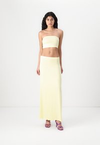 Yellow strapless crop top paired with a matching long skirt. Fabric appears smooth and stretchy, accentuated by purple heeled sandals.