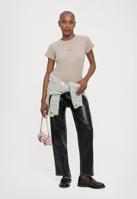 Beige cotton t-shirt, black leather wide-leg pants, light grey knit sweater tied at the waist, and a small pink handbag.