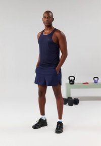 Marinblå atletisk linne och shorts, slimmad design, ventilerande tyg, sidogrepp för rörlighet, kombinerat med svarta sportskor och vita strumpor.