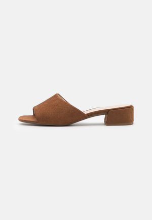 Mules en daim brun avec un orteil ouvert, un design supérieur incliné et un petit talon bloc, présentant une texture douce et un style minimaliste.