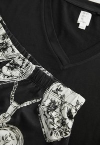 Haut noir col en V avec short élastique à taille blanche imprimée, arborant des motifs floraux et de pendentifs chaînés. L’étiquette indique « NEXT time to dream. »