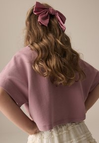 Korte mouwen, loszittend shirt van zacht mauve stof met een getextureerd oppervlak en een cropped zoom, aangevuld met een groot haarstrikaccessoire.