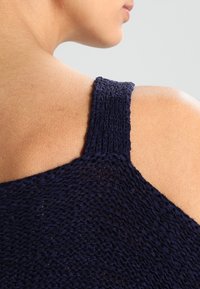 Marinblå stickad topp med ett strukturerat mönster och bred axelrem, har en rundad halsringning och design med öppna axlar.