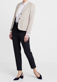 Beige lněný blazer se dvěma knoflíky, kombinovaný s pruhovanými námořnickými kalhotami a středně vysokými námořnickými botami s otevřeným zadním dílem.